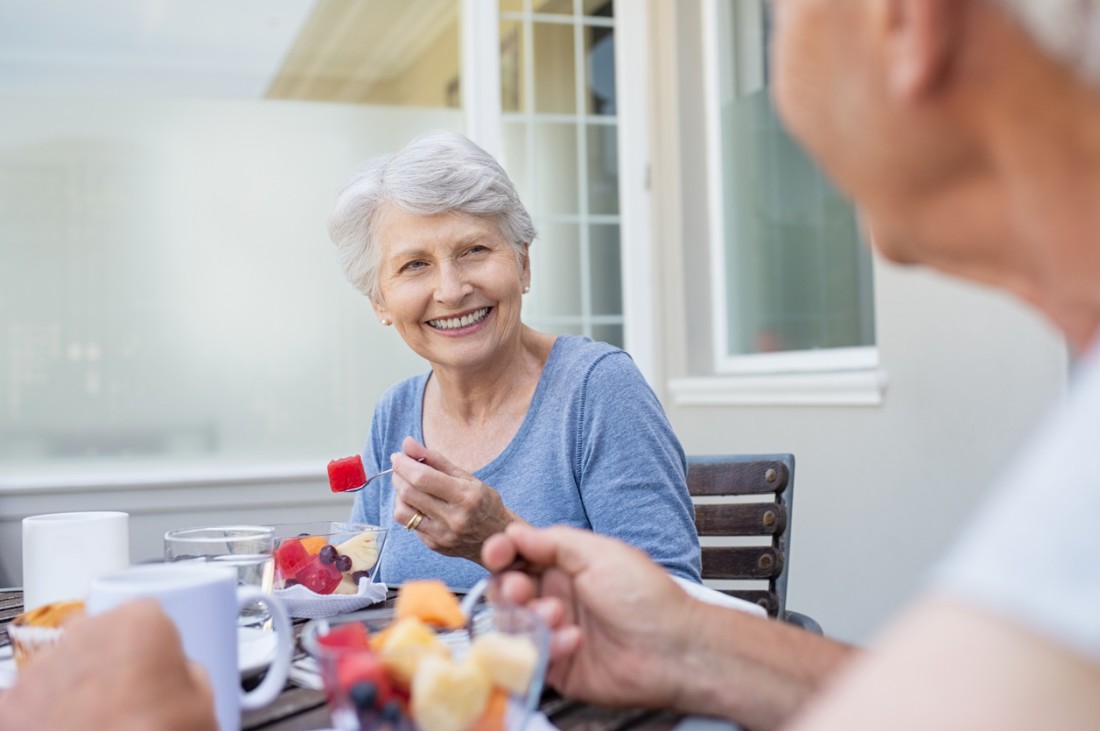 Happy older woman eating fresh fruits during breakfast