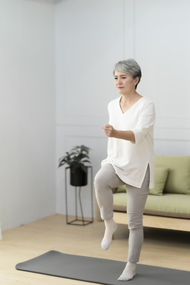 An older woman marches in place on a yoga mat at home