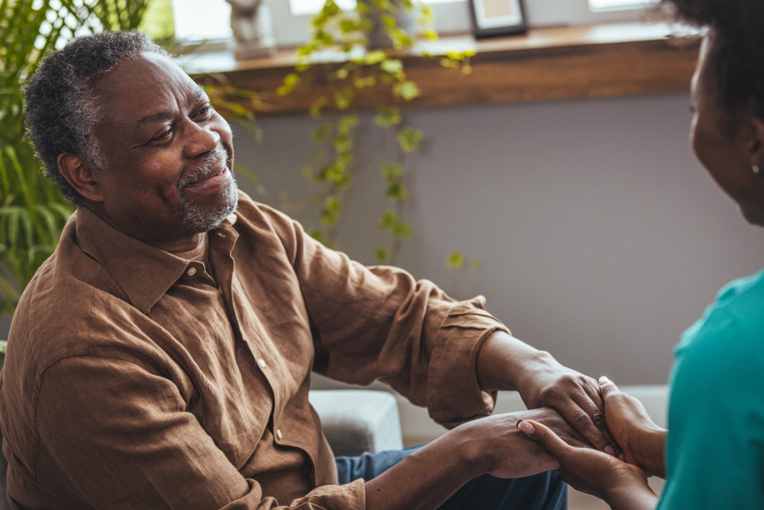 An older man holds hands with his companion care service provider