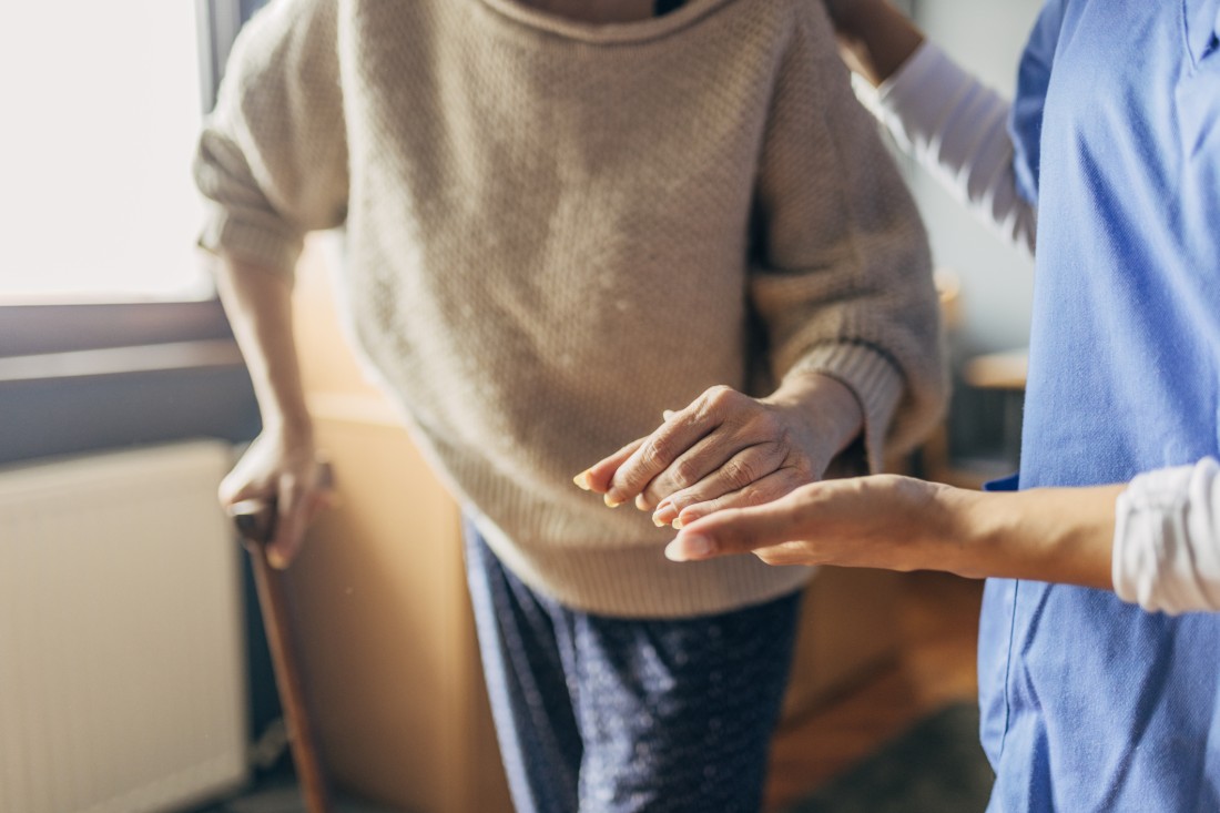 A caregiver helps an older adult use a walking aid